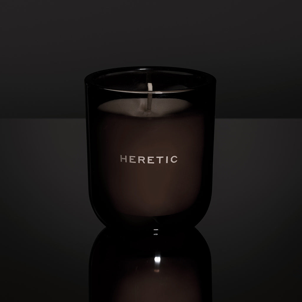 Candle in a black container with 'HERETIC' text on a dark background