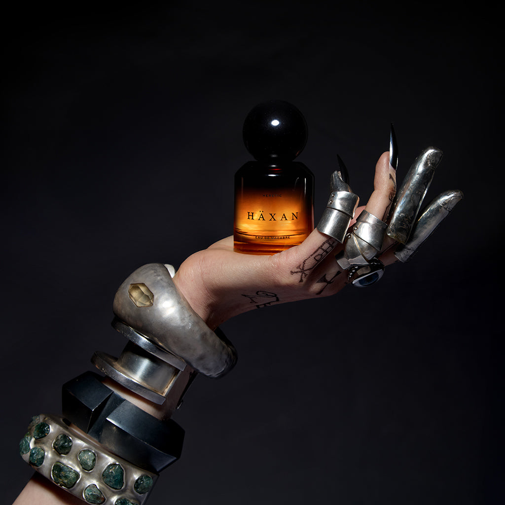 Hand holding a bottle of Haxan perfume against a dark background
