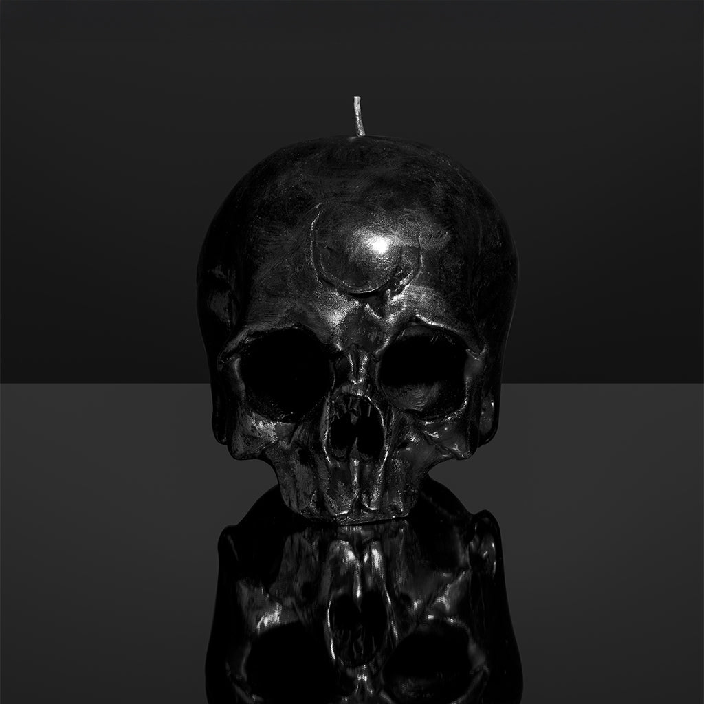 Black skull-shaped candle on a reflective surface with a dark background